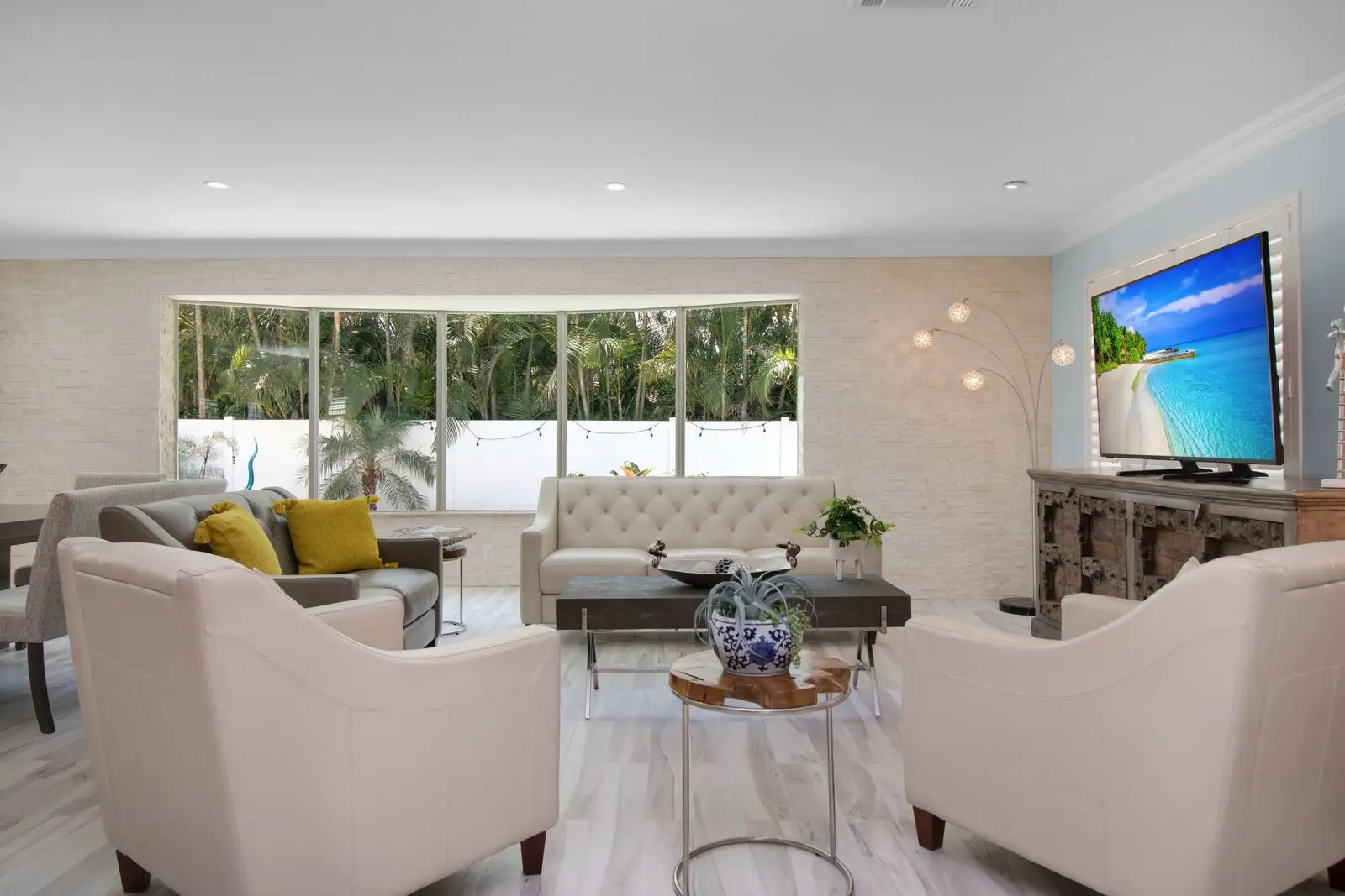 Bright living room in a furnished rental home, with cream armchairs and a wide window onto palm trees