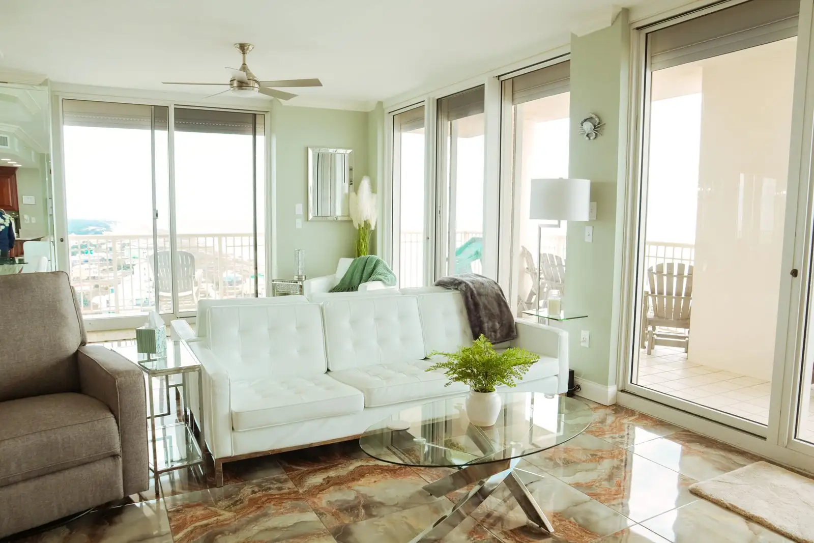 Light-filled condo living room with a white sofa, ceiling fan and balcony doors — vacation rental photography